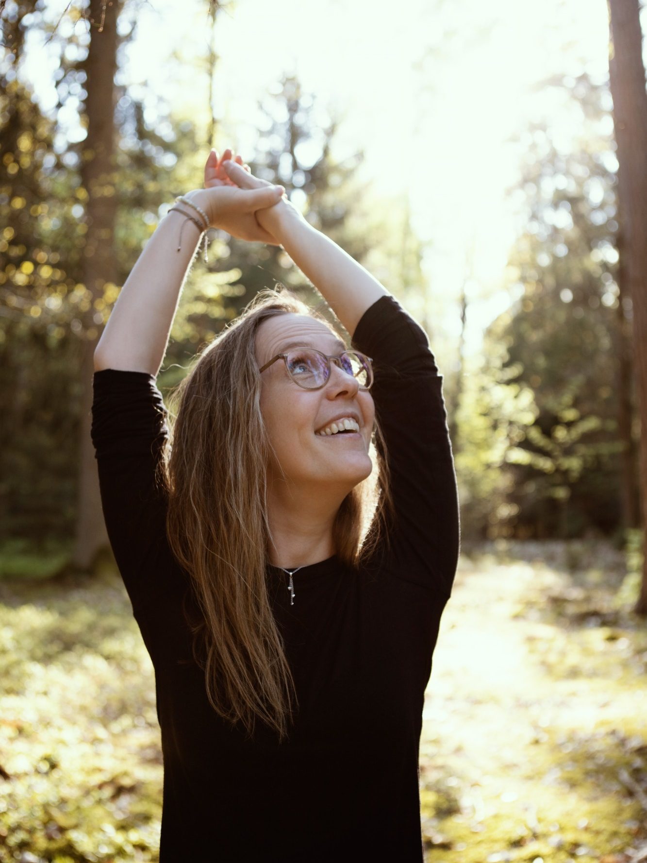 Zufriedenheit Frau mit langen Haaren hebt die Arme in einem sonnigen Waldgebiet.